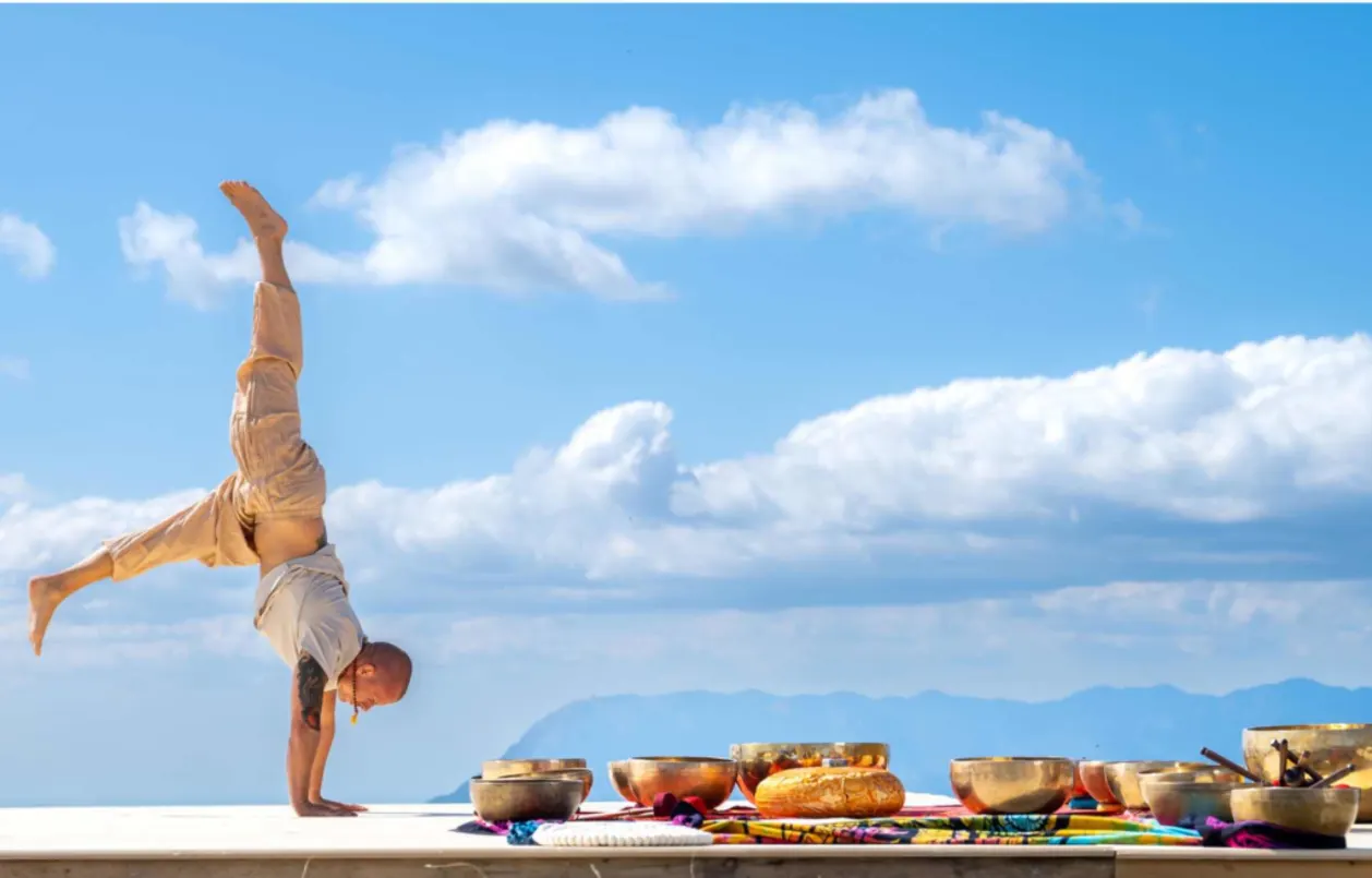 man doing handstand with sound healing bowls nearby